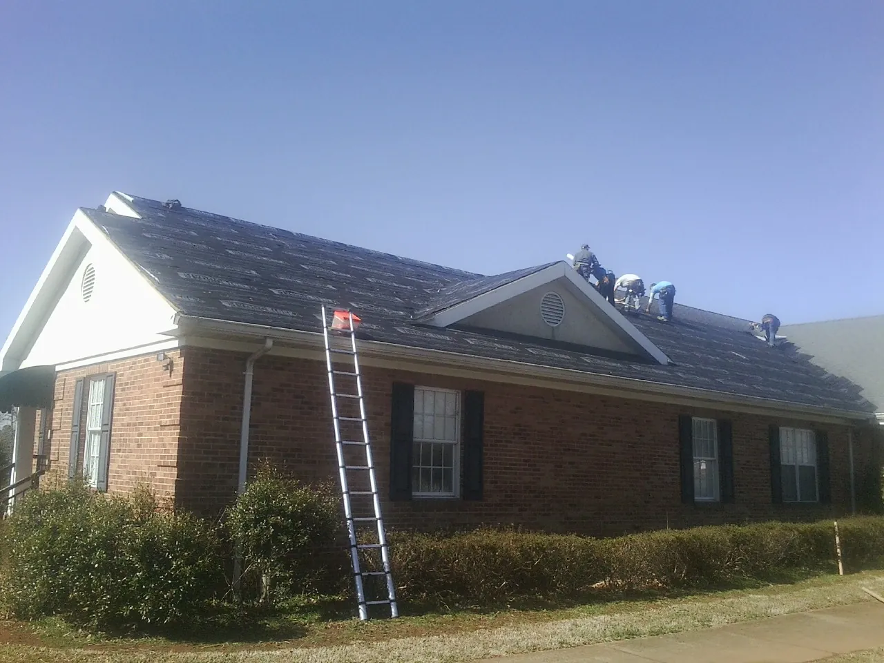 Crew tearing shingles off a brick ranch roof with a ladder set — Metal Roof Repair work by our crew in Armona