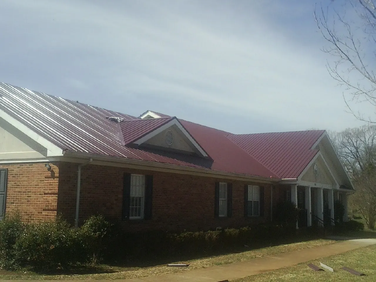 Red metal roof with gabled entries on a long brick building, from a Hail Damage Roof Repair job in Armona