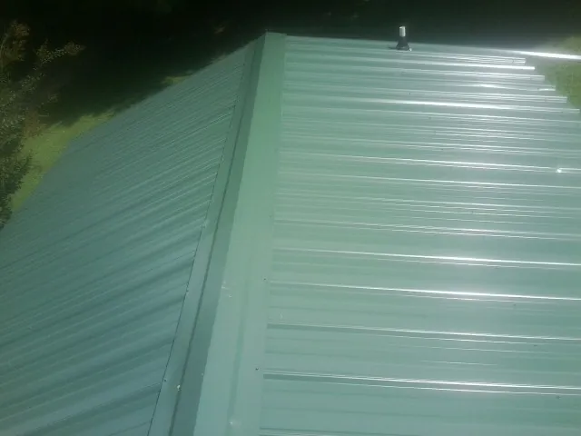 New green metal panels meeting at the ridge of a roof — Flat Roof Repair work by our crew in Armona