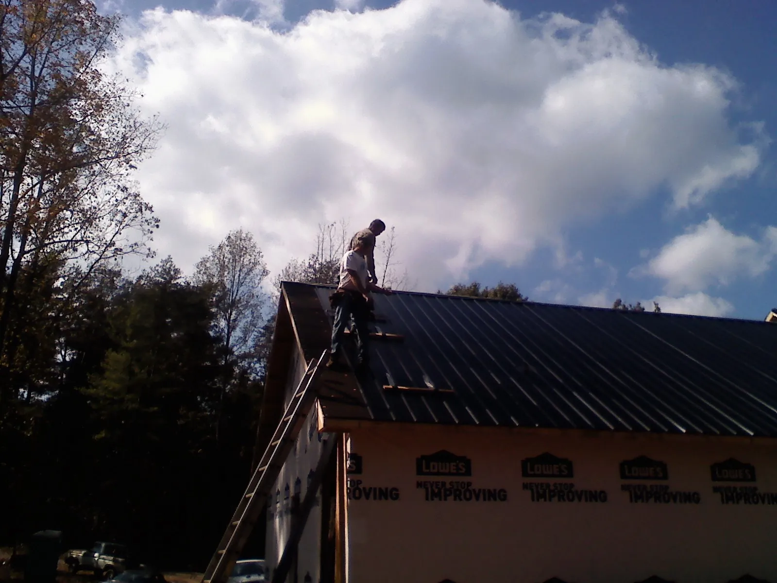 Roofer fastening dark metal panels high against a cloudy sky, from a Roof Inspection job in Armona
