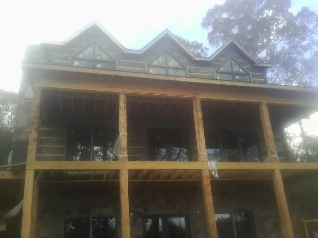 Dormers and porch framing on a large log home under construction — Roof Coating work by our crew in Armona