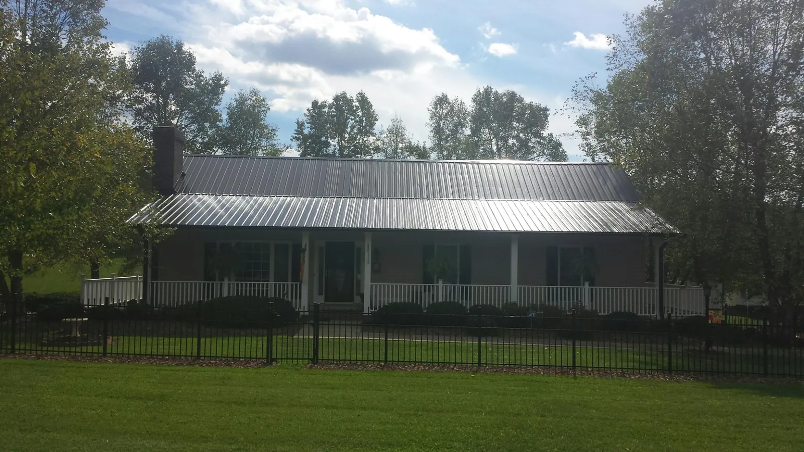 Gray metal roof on a brick ranch with a full width front porch — Gutter Guard Installation work by our crew in Armona