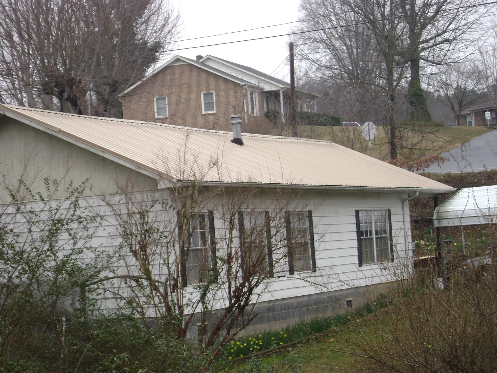 Tan metal roof on a white sided house set into a hillside — Commercial Roofing by Roofing Brothers in Armona